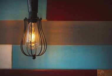 Çağdaş bir ahşap duvardan sarkan antika bir ampul armatürünün görüntüsü.
