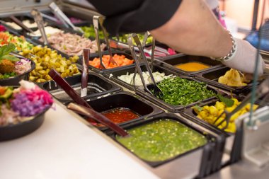 Restoran yemeklerinin çeşitli özelleştirilmiş malzemelerle sergilendiği bir manzara. Bir çalışan kase siparişi hazırlar..