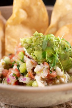 Bir kase ceviche yakın çekim, guacamole ile süslenmiş ve bir dizi bol yağda kızartılmış tortilla, bir restoranda veya mutfak ortamında.