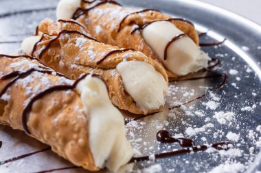 Gümüş tepside, bir restoranda ya da mutfak ortamında üç küçük cannoli tatlısının yakın plan görüntüsü.
