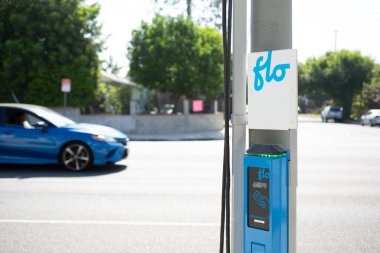 Los Angeles, California, ABD - 07-03-2021: Bir caddenin kenarına kurulmuş FLO elektrikli araç şarj istasyonu manzarası. Caddede bir araba geçiyor..