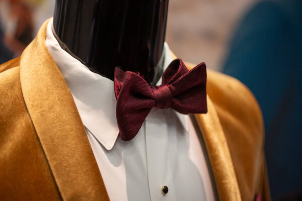 A view of a crimson colored bow tie, part of an elegant male tuxedo ensemble on a manikin.