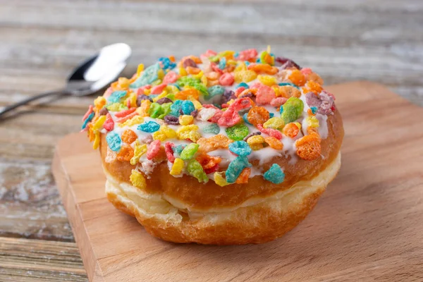 A view of a donut with white icing and colorful pebble cereal toppings.
