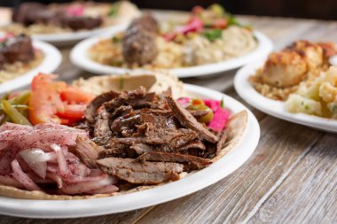 Ahşap bir masa yüzeyindeki birkaç Akdeniz antresinin manzarası, sığır eti shawarma içerir..