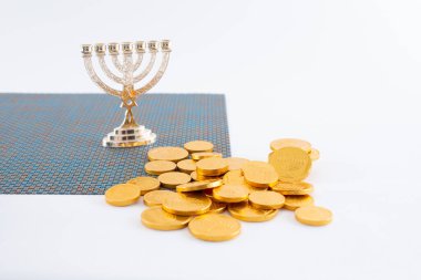 Beyaz bir zemin üzerinde küçük bir menorah süsü ile süslenmiş çikolata sikkeleri yığını manzarası.