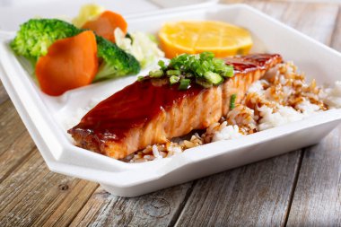 Teriyaki somonu ve pirinç kombinasyonlu konteynır manzarası.