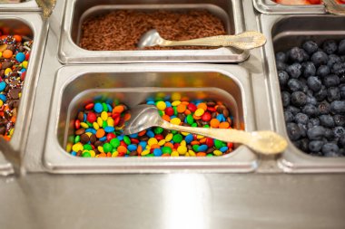 Yerel bir dondurmacıda veya donmuş yoğurt dükkanında bulunan ve içinde yaban mersini, çikolata parçacıkları ve çikolata parçacıkları bulunan çok sayıda popüler malzemeyi görmek.