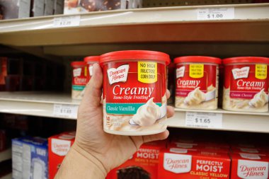 Long Beach, California, United States - 02-12-2020: A hand holds a container of Duncan Hines Creamy Home-Style Frosting, on display at a local grocery store.