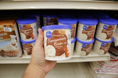 Long Beach, California, United States - 02-12-2020: A hand holds a container of Pillsbury Creamy Supreme Cinnamon Bun Frosting, on display at a local grocery store.