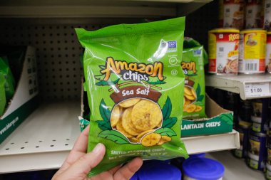 Long Beach, California / ABD - 02 / 12 / 2020: Yerel bir bakkalda sergilenen Amazon tuzlu muz cipsi paketini bir el tutuyor.