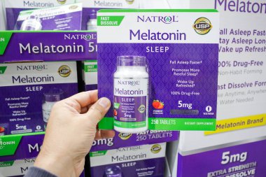 Alhambra, California, ABD - 02-19-2020: Bir el, yerel büyük bir market vitrininde sergilenen bir paket Natrol Melatonin diyet ilavesi tutuyor.