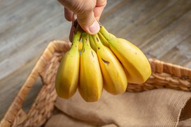 Muz kümesini sepetin üzerinde tutan bir elin görüntüsü.