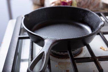 A view of a cast iron skillet on a stove top, in a kitchen setting.