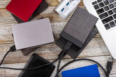 A top down view of several external hard drives next to a laptop computer, on a wooden surface.