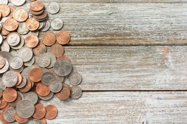 A top down view of a pile of United States coin currency on a wooden surface on the left side of the frame.