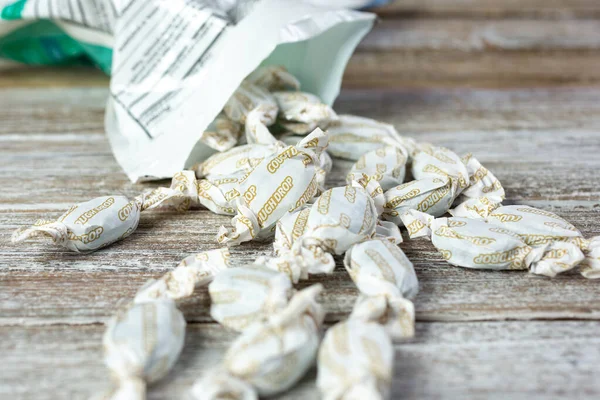 A closeup view of a pile of cough drops falling out of its open package, on a wooden surface.