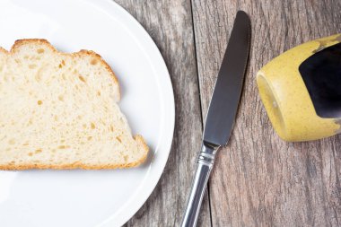 Ahşap bir yüzey üzerinde bir tabak ekşi ekmek dilimi, bir bıçak ve bir şişe hardal..
