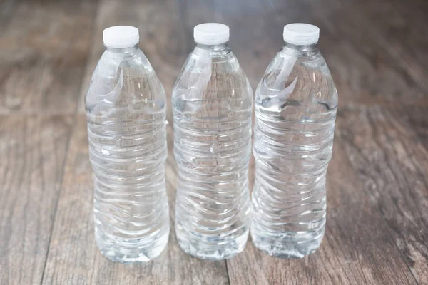 A view of three plastic water bottles without any labels, on a wooden surface.