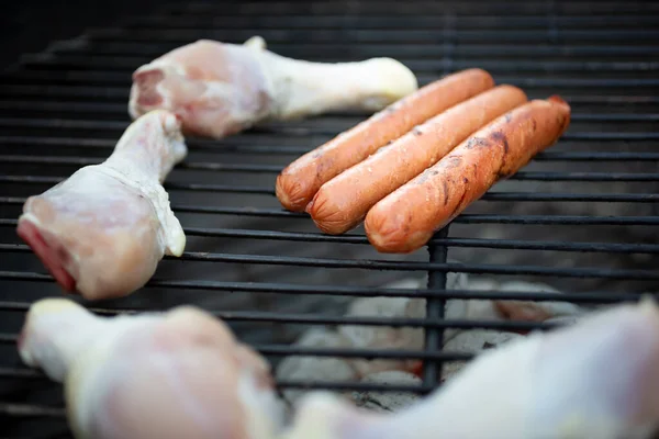 几个热狗和鸡腿在烤肉架上烹调的特写镜头 — 图库照片