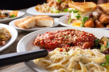 Bir tabak parmesanlı tavuk ve makarna içeren, hazırlanmış birkaç başlangıç yemeğinin bir görüntüsü..