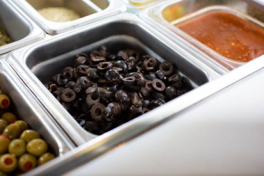 Dilimlenmiş siyah zeytinli bir malzeme istasyonu görüntüsü.