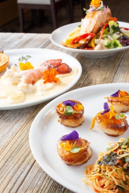 Deniz ürünleri, deniz tarakları, ıstakoz kuyruğu ve somon balığı içeren çeşitli gurme manzarası.