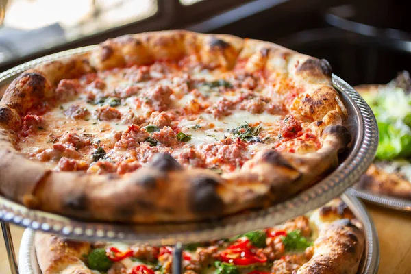 Doğal ışık alan bir pencerenin yanındaki restoranda sergilenen ve sosisli bir pizzanın yer aldığı birkaç rustik pizza manzarası..