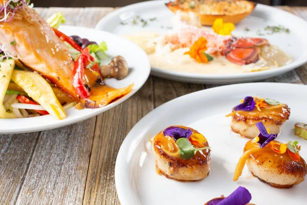 Deniz ürünleri, deniz tarakları, ıstakoz kuyruğu ve somon balığı içeren çeşitli gurme manzarası.