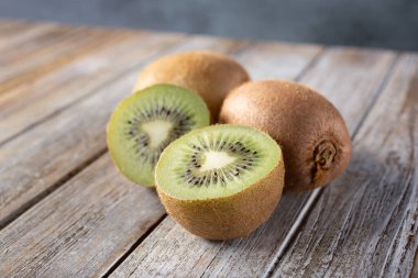 Ahşap bir masa yüzeyindeki kivi manzarası, içinde tüm meyve ve bir meyve kesiği var..