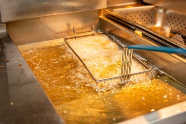 A closeup view of a food basket frying in bubbling oil, in a restaurant kitchen setting.