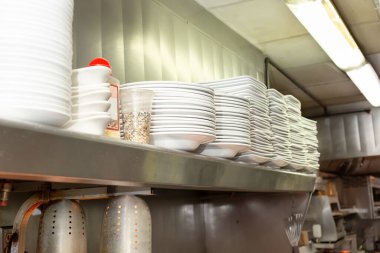 Restoranın mutfak ortamında, üzerinde beyaz tabaklar bulunan bir raf manzarası..