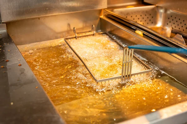A closeup view of a food basket frying in bubbling oil, in a restaurant kitchen setting.