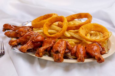 Bufalo kanatları, soğan halkaları ve patates kızartmalarıyla aperatif bir tabak..