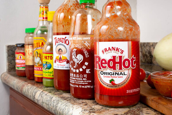 Los Angeles, California, United States - 06-09-2020:A view of a counter with a row of popular hot sauce bottles, featuring Frank's RedHot, Huy Fong Foods sriracha, Tapatio, El Pato, and Cholula.