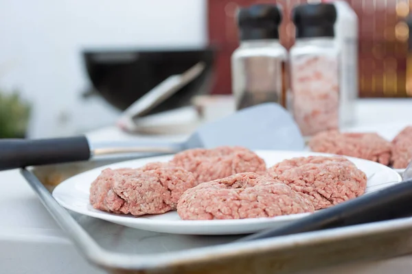 A view of several raw burger patties on a plate, ready for grilling.