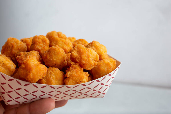 A view of a hand holding a tray of chicken nuggets.