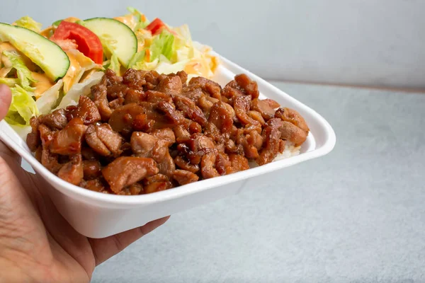 Tavuklu teriyaki kombinasyonlu tabağı köpüklü kapta tutan bir el görüntüsü..
