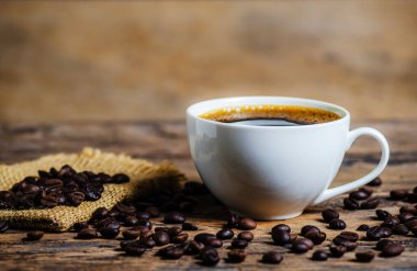 Bir fincan kahve, kahve çekirdeği ve ahşap arka planda koyu ton dtyle.