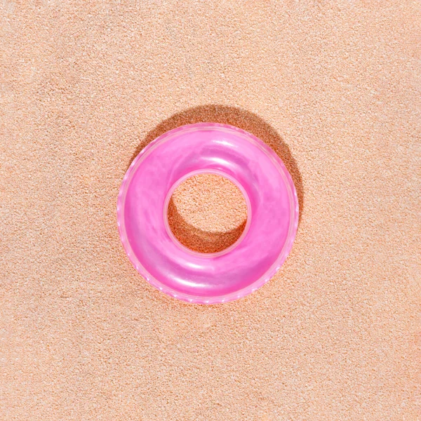 Pink swimming ring or pool toy on sandy summer beach. Minimal holiday concept with sharp sunny shadow with sand texture. Above view. Flat lay.