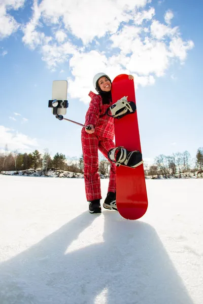 Donna con lo snowboard utilizzando smartphone su un bastone per fare selfie — Foto Stock