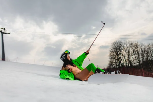 Piękna kobieta używająca smartfona do robienia selfie z snowboardem na stoku narciarskim — Zdjęcie stockowe