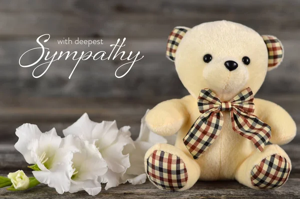 Condolences card with teddy bear and white flower on wooden background