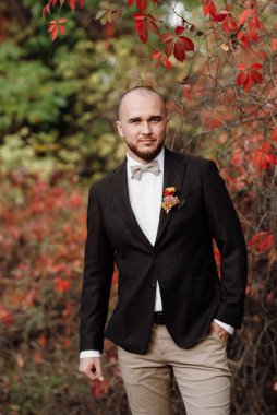 Kızıl üzümlerin arka planında kahverengi ceketli kel sakallı adam.