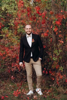 Kızıl üzümlerin arka planında kahverengi ceketli kel sakallı adam.