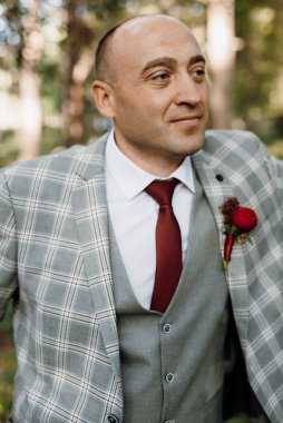 Yeşil ormanın arka planında gri ceketli kel bir adam.