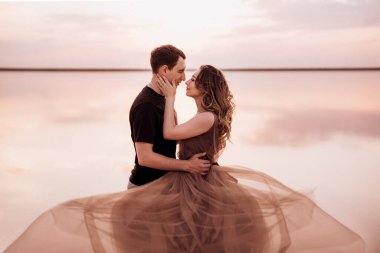 Gün batımında pembe tuz gölünün kıyısında bir adam ve bir kız.