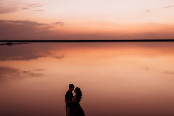 日落时分 一个女孩和一个男人在一个粉色盐湖畔 — 图库照片