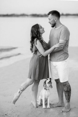 Boş kumsalda, turuncu elbiseli, köpekli genç bir çift.