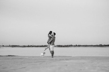 Boş kumsalda, turuncu elbiseli, köpekli genç bir çift.