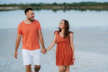 Boş kumsalda, turuncu elbiseli, köpekli genç bir çift.